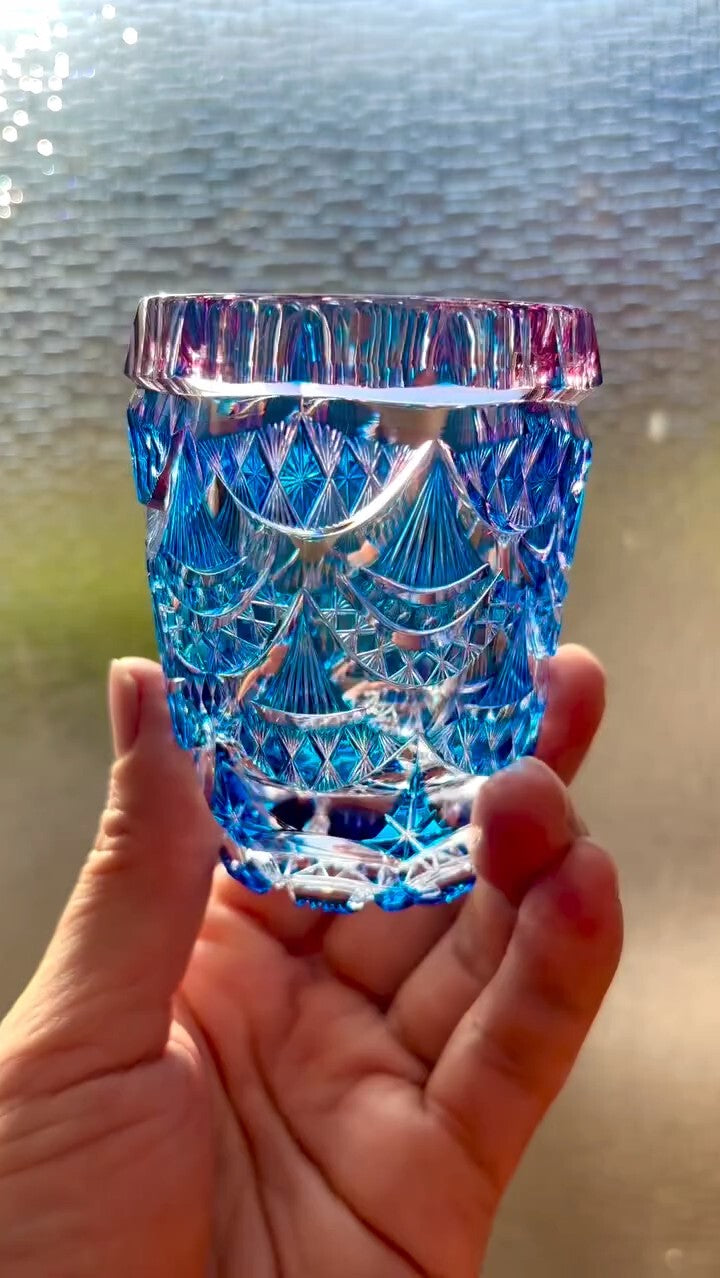 Cut-glass tumbler held up to the light, deep blue and violet facets throwing bright patterns.