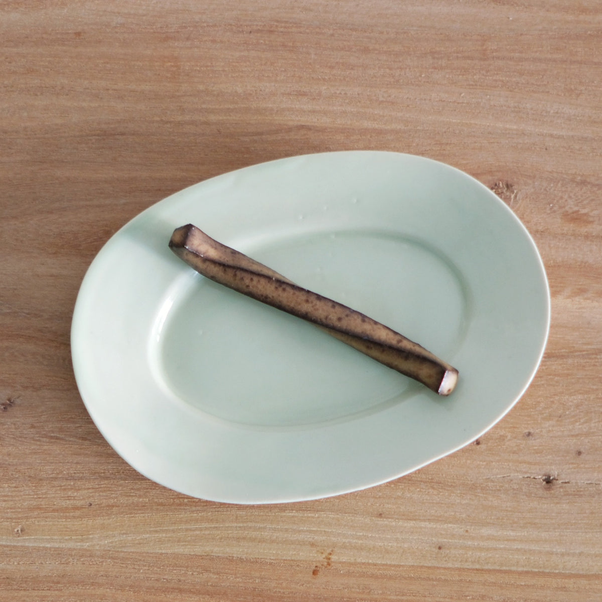 Small pale celadon leaf-shaped rest holding a dark wooden chopstick, on a wooden table.