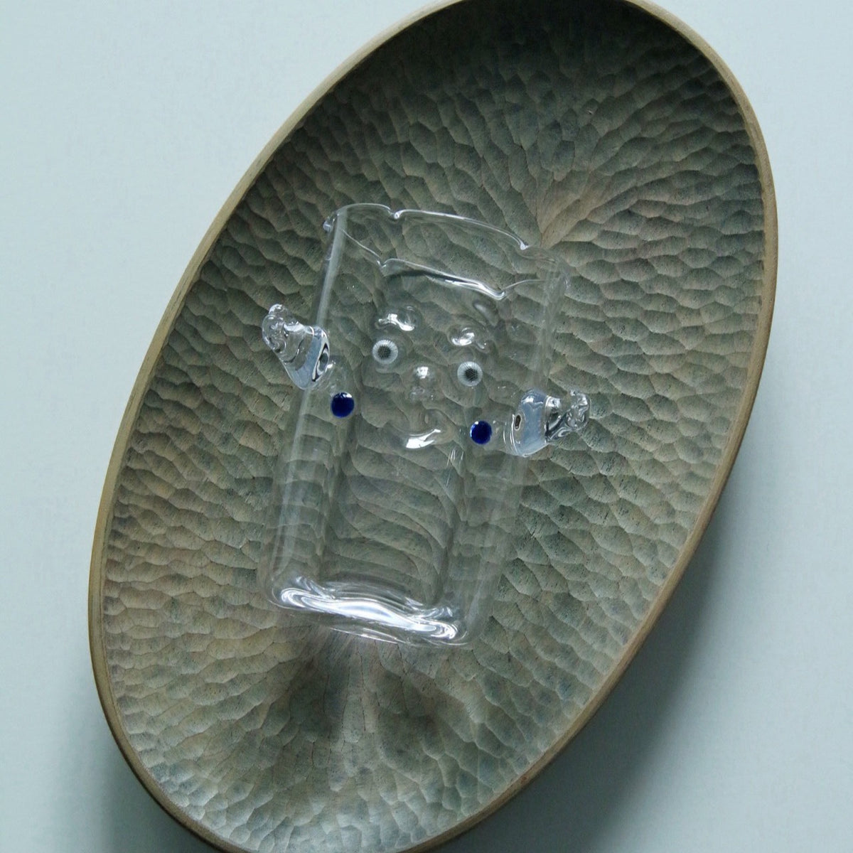 Clear glass cup with a small applied glass creature clinging to its side, on a green dimpled plate.