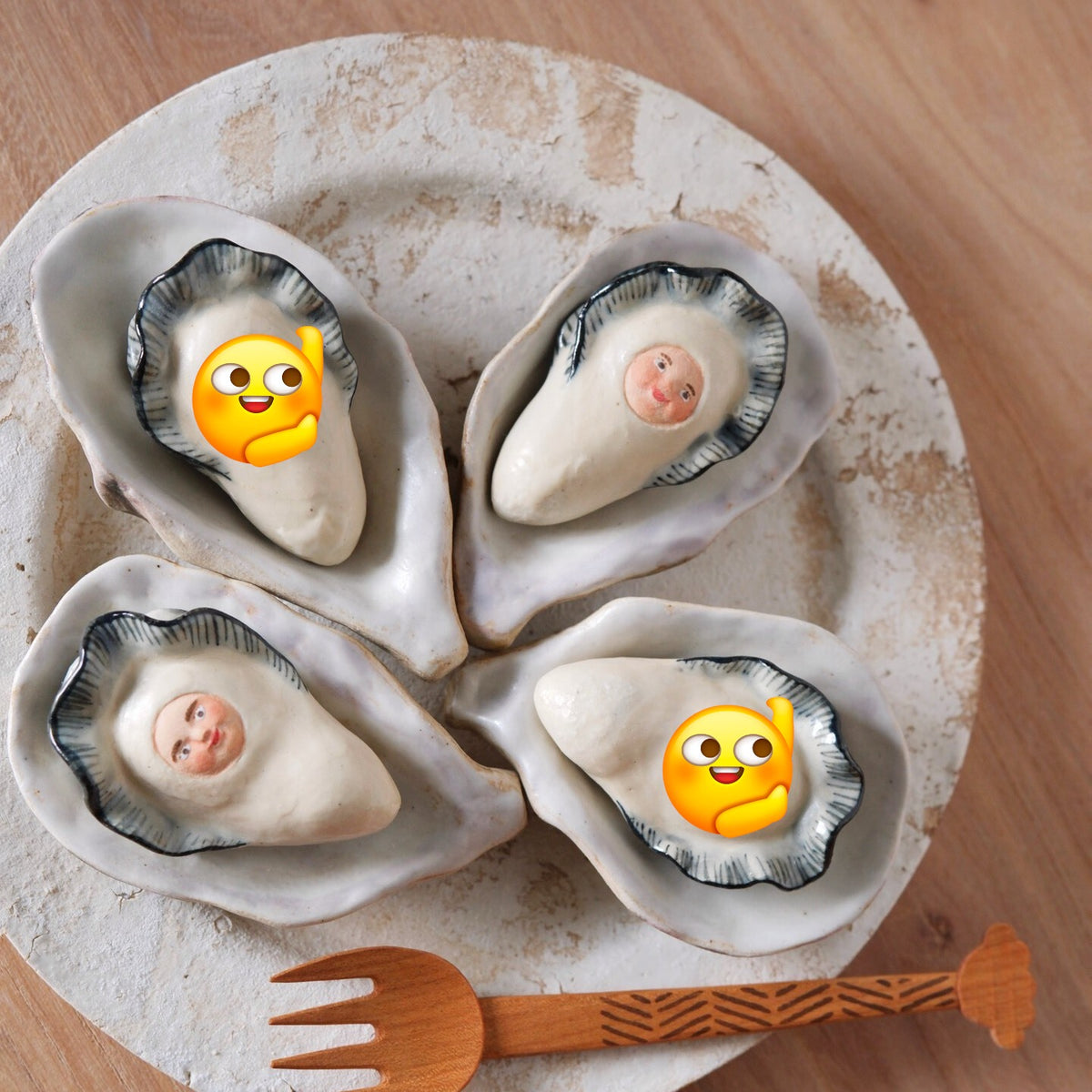 Four ceramic oyster shells, each holding a small pearl-like figure with a painted face.