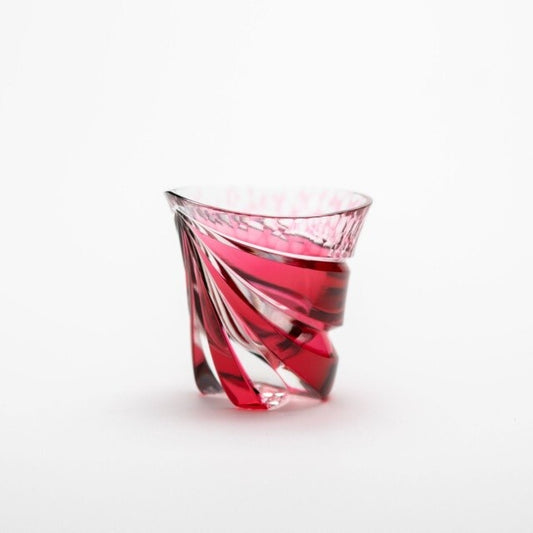 Small cut-glass sake cup in deep red and clear, its twisted facets flaring out towards the rim.