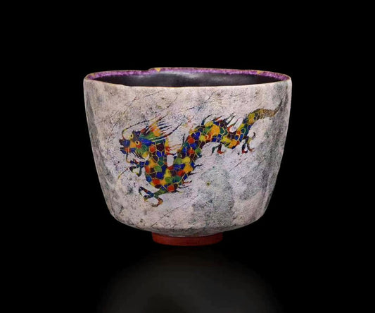 Pale speckled faceted tea bowl painted with a long multicoloured dragon, standing on a red foot ring.