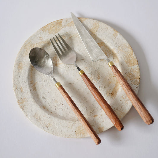 A spoon, fork and knife with wooden handles laid across a speckled cream plate.