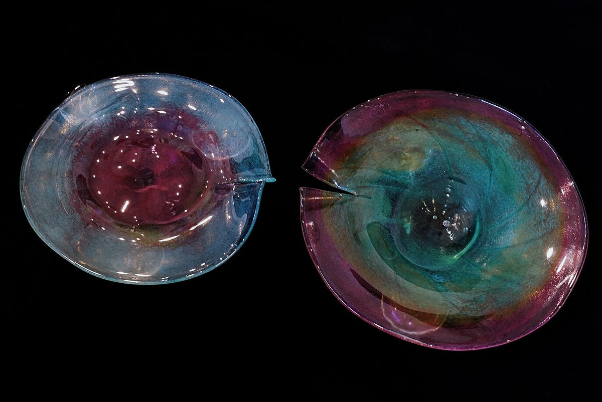 Two iridescent glass leaf-shaped plates, one swirled pink and violet, the other turquoise and gold.