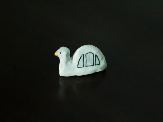 Small white porcelain bird rest with a yellow beak and two blue wing marks, lit against black.