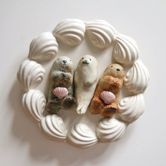 Three small ceramic seals lying on their backs, ringed by a wreath of pale ceramic waves.