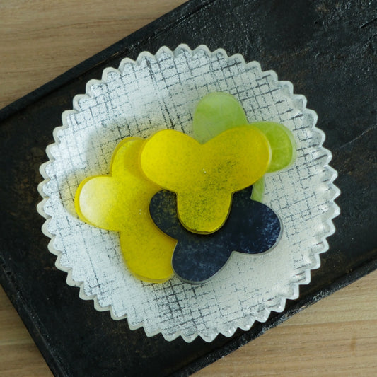 Flower-shaped glass chopstick rests in yellow, green and deep blue on a frosted glass plate.