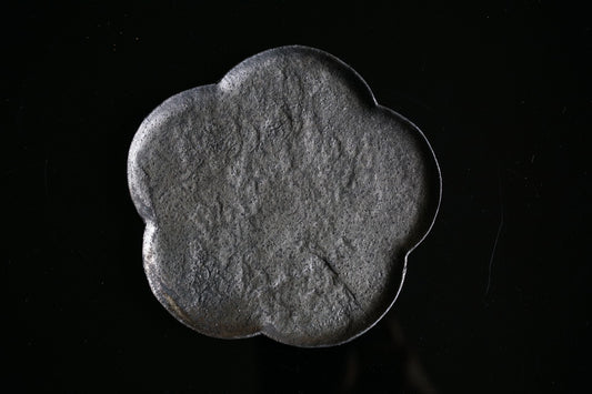 Plum-blossom shaped dish in matte grey with a coarse stone-like surface, lit against black.