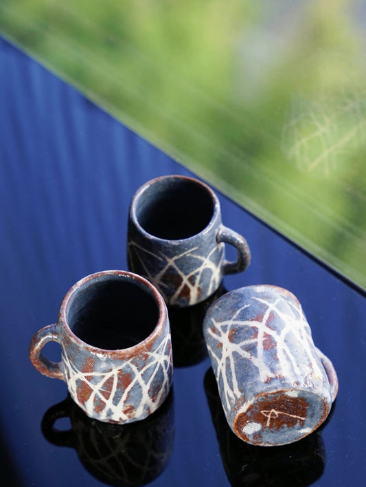 Three cups with dark interiors and rust-brown outsides brushed with loose white lines, on a deep blue ground.