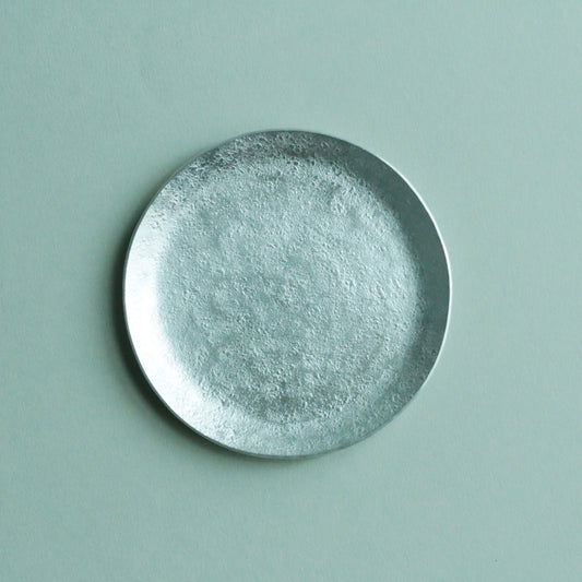 Small round aluminium plate with a lightly hammered surface, on a pale green ground.