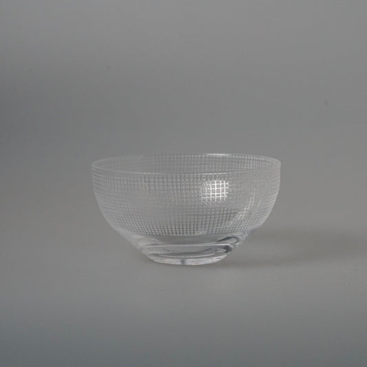 Clear glass bowl with a fine woven grid pressed into its walls, on a pale grey ground.