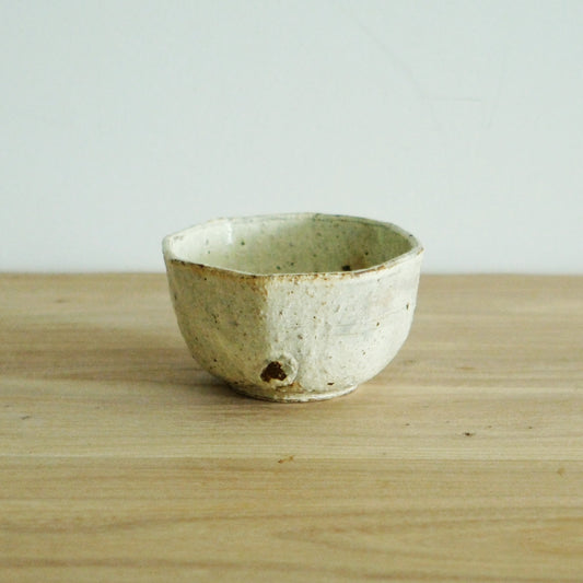 Small octagonal bowl in speckled cream with a rust-marked rim, on a light wooden table.
