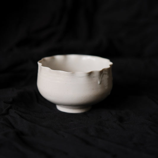 White porcelain bowl on a low foot, its rim rising and falling in soft torn scallops.