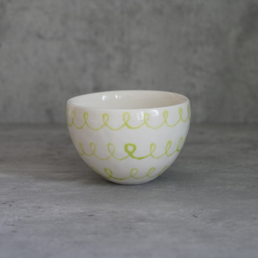 White bowl painted with a band of looping yellow-green scribbles below the rim.