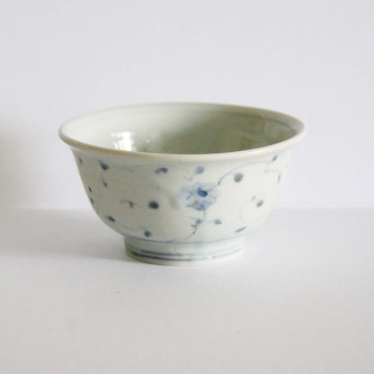 White footed rice bowl scattered with small blue painted blossoms and a fine ringed foot.