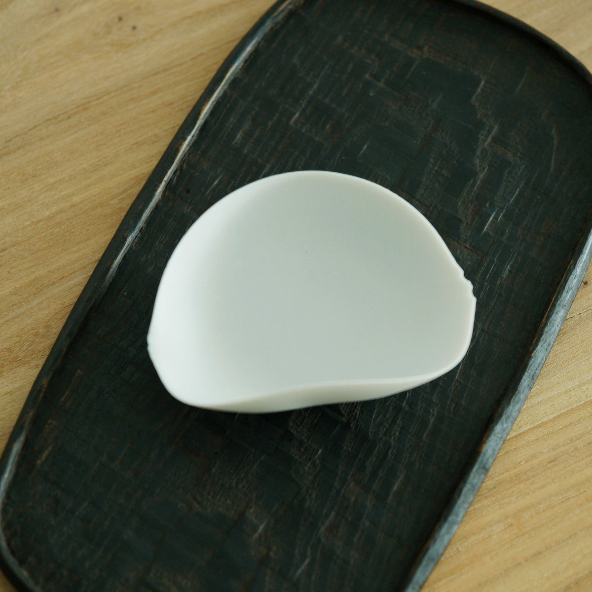 Curved white porcelain tea leaf holder shaped like a folded shell, on a dark board.