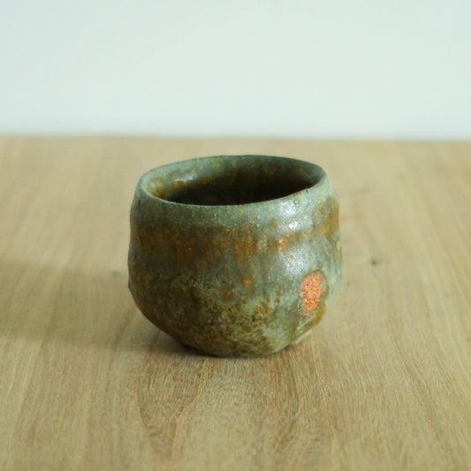 Small tea cup in mottled olive green with warm orange blushes breaking through the glaze.
