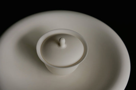 White porcelain lidded bowl with a small pointed knob, sitting on a matching white saucer.