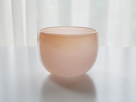 Rounded opaque glass bowl in pale blush pink, glowing against a bright white curtain.