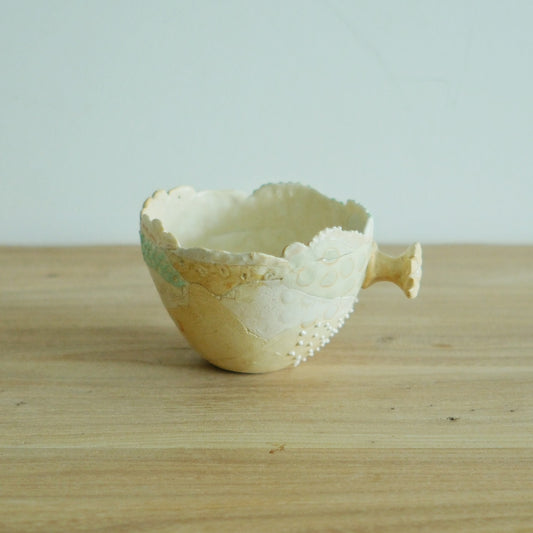 Wide cream mug with a frilled lace rim, a small spurred handle and a finely carved body.