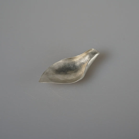 Small tin tea scoop folded into a soft leaf shape, its bright surface catching the light.