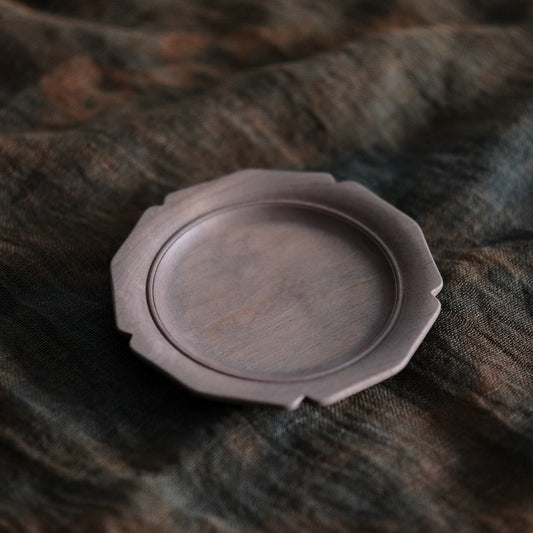 Small round wooden plate with a softly scalloped edge and a shallow well, on brown cloth.