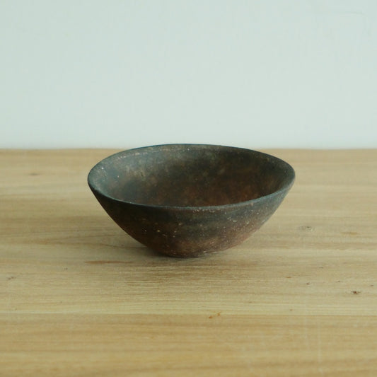 Small conical rice bowl in dark mottled brown-grey, seen from the side on a wooden table.