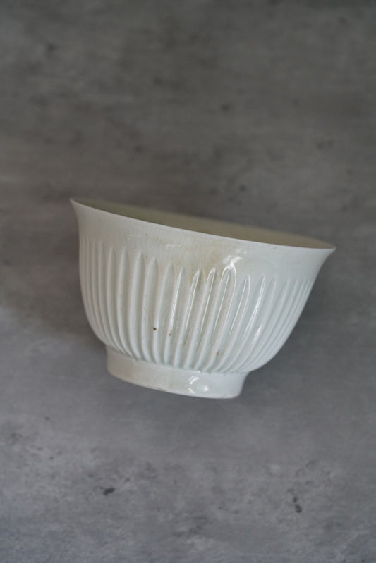 White porcelain bowl with close vertical ribbing and a softly torn scalloped rim.
