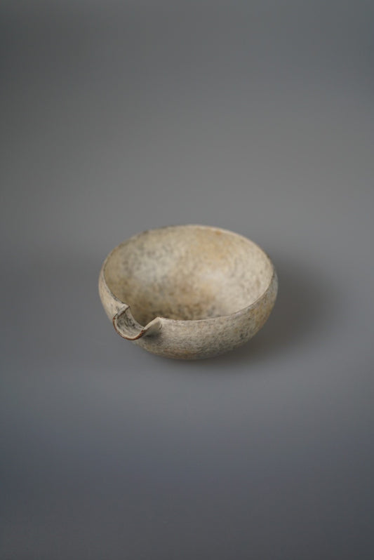 Low round pouring bowl in speckled sandy cream with a small pinched spout.