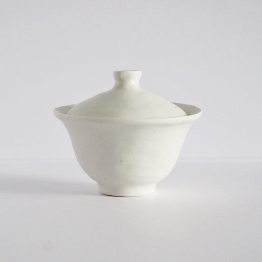 White porcelain lidded tea bowl with a domed lid and a wide flared rim beneath it.