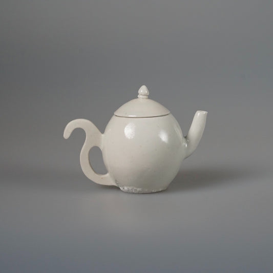 Small white porcelain teapot with a knopped lid, a slender spout and a curled handle.