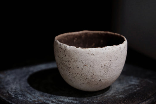 Egg-shaped tea bowl in rough cream white slip, heavily speckled, with a darker unglazed foot.
