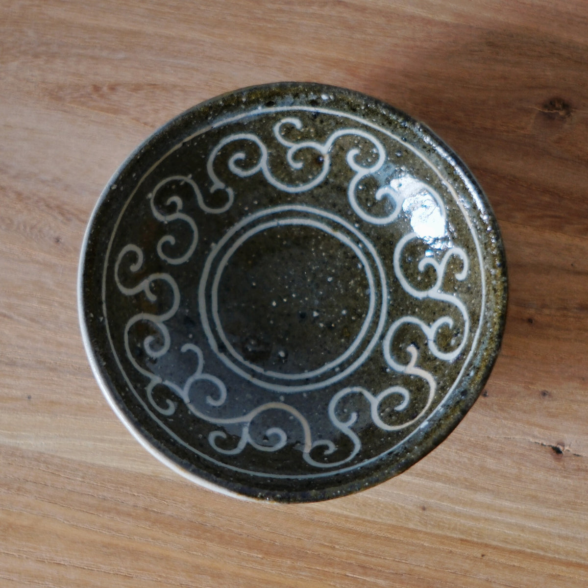 Small dark dish inlaid with a ring of white scrolling curls around its glossy black centre.