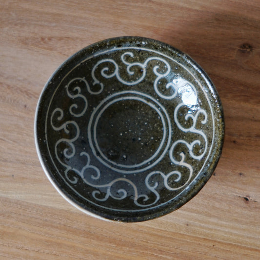 Small dark dish inlaid with a ring of white scrolling curls around its glossy black centre.