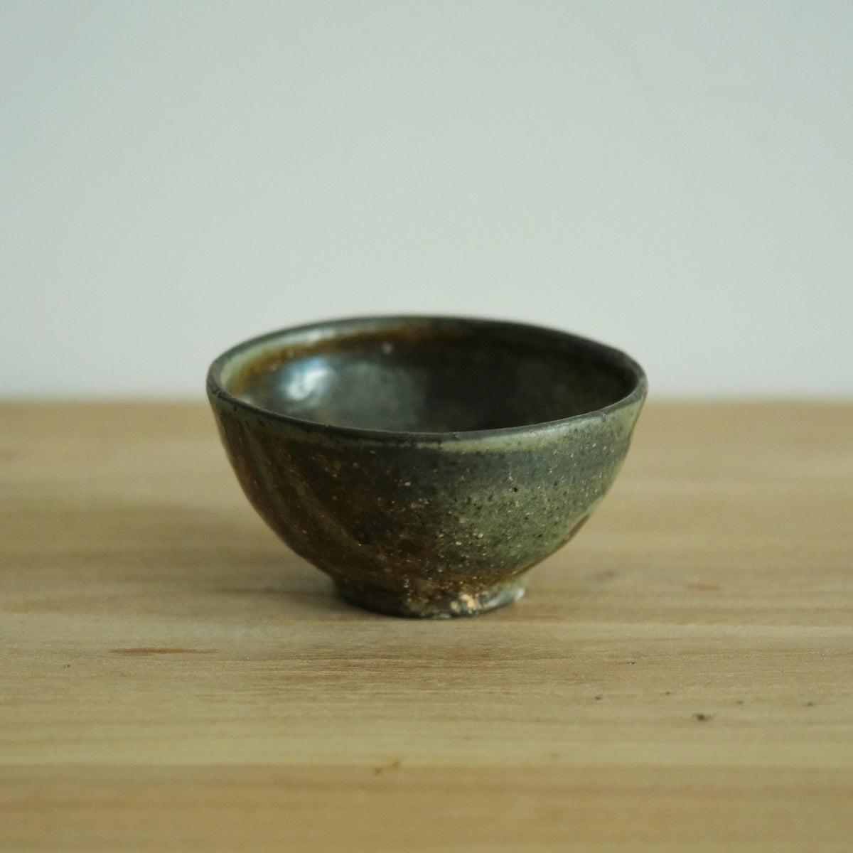 Footed rice bowl in deep olive wood-fired glaze with warm brown breaking through at the rim.
