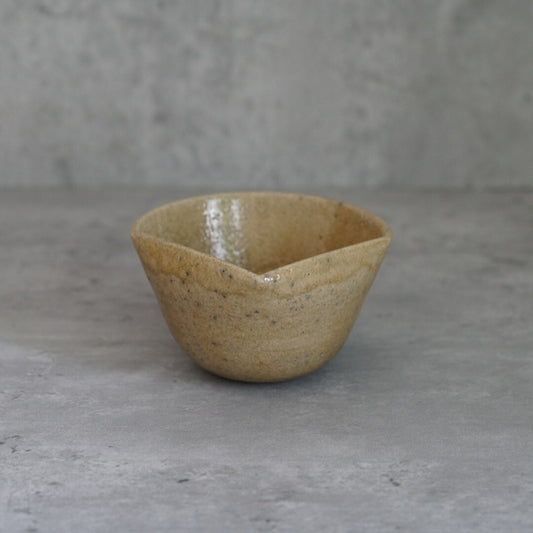 Conical bowl in speckled ochre with straight flaring walls, on grey concrete.