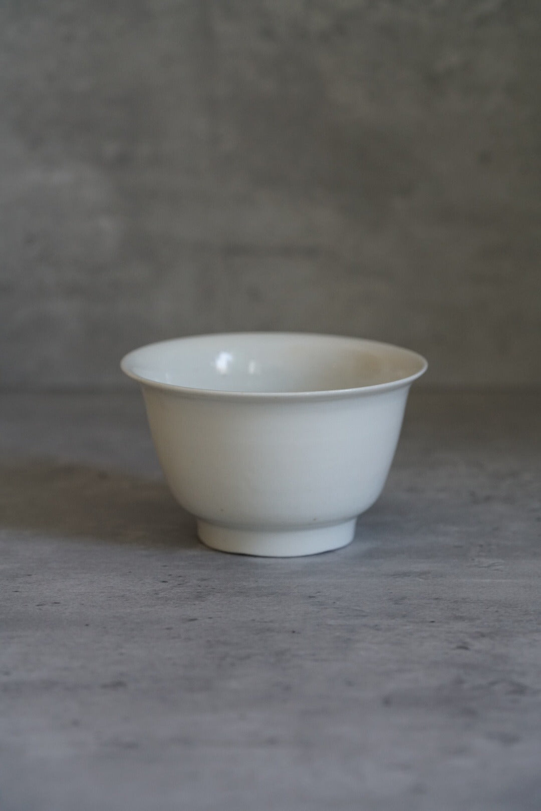 Plain white porcelain bowl on a small foot, its thin walls flaring to a clean rim.