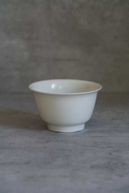 Plain white porcelain bowl on a small foot, its thin walls flaring to a clean rim.