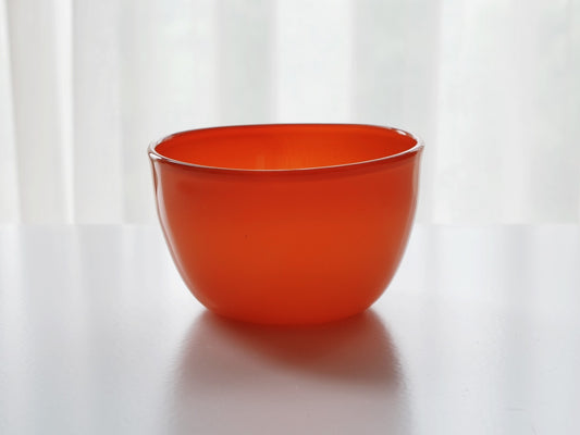 Deep glass bowl in vivid orange-red, its rim thinning to a pale translucent edge.
