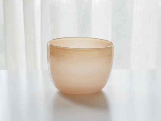 Rounded frosted glass bowl in soft peach cream, against a bright white curtain.