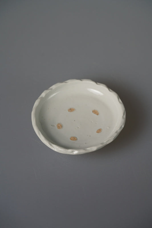 Small white porcelain plate with a softly scalloped rim and a few pale firing marks.