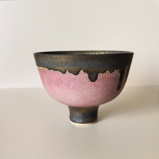 Footed tea bowl with a wide pink band, the dark bronze rim running down in soft drips.