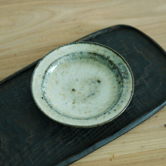 Small round dish with a soft cream glazed well and a rust-brown rim, on a dark board.