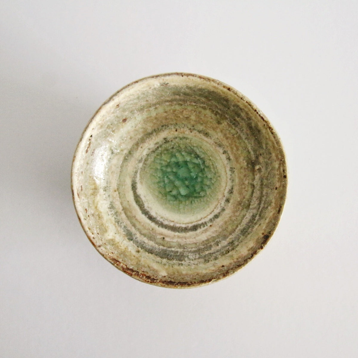Small cream rice bowl seen from above with a bright jade green pool at its centre.