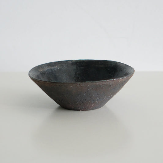 Conical rice bowl with a dark glazed rim fading to bare rust-brown clay at the foot.