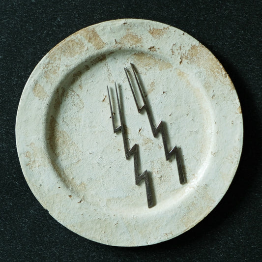Three dark slim forks with zigzag handles, arranged on a speckled cream plate.