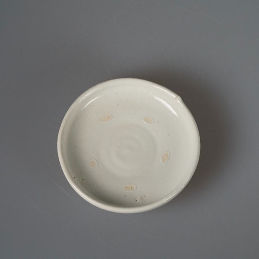 Shallow white porcelain plate with faint throwing rings and a few amber firing spots.