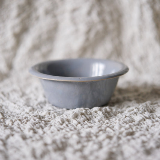 Small grey bowl with a folded outward rim, resting on rough cream cloth.