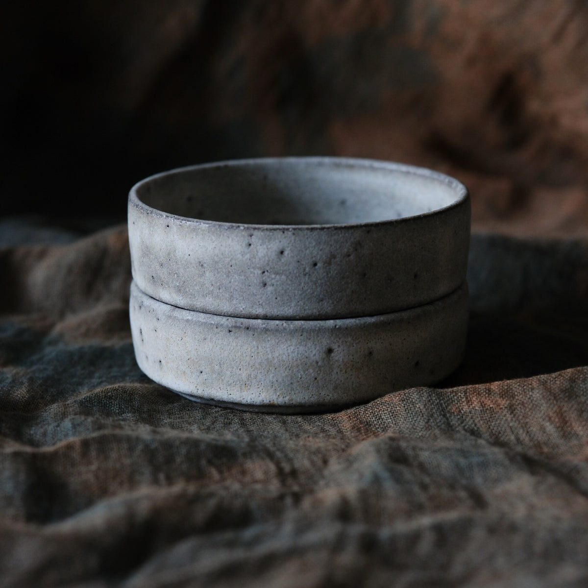 Two shallow speckled grey bowls stacked on rumpled dark brown cloth.