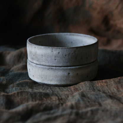 Two shallow speckled grey bowls stacked on rumpled dark brown cloth.